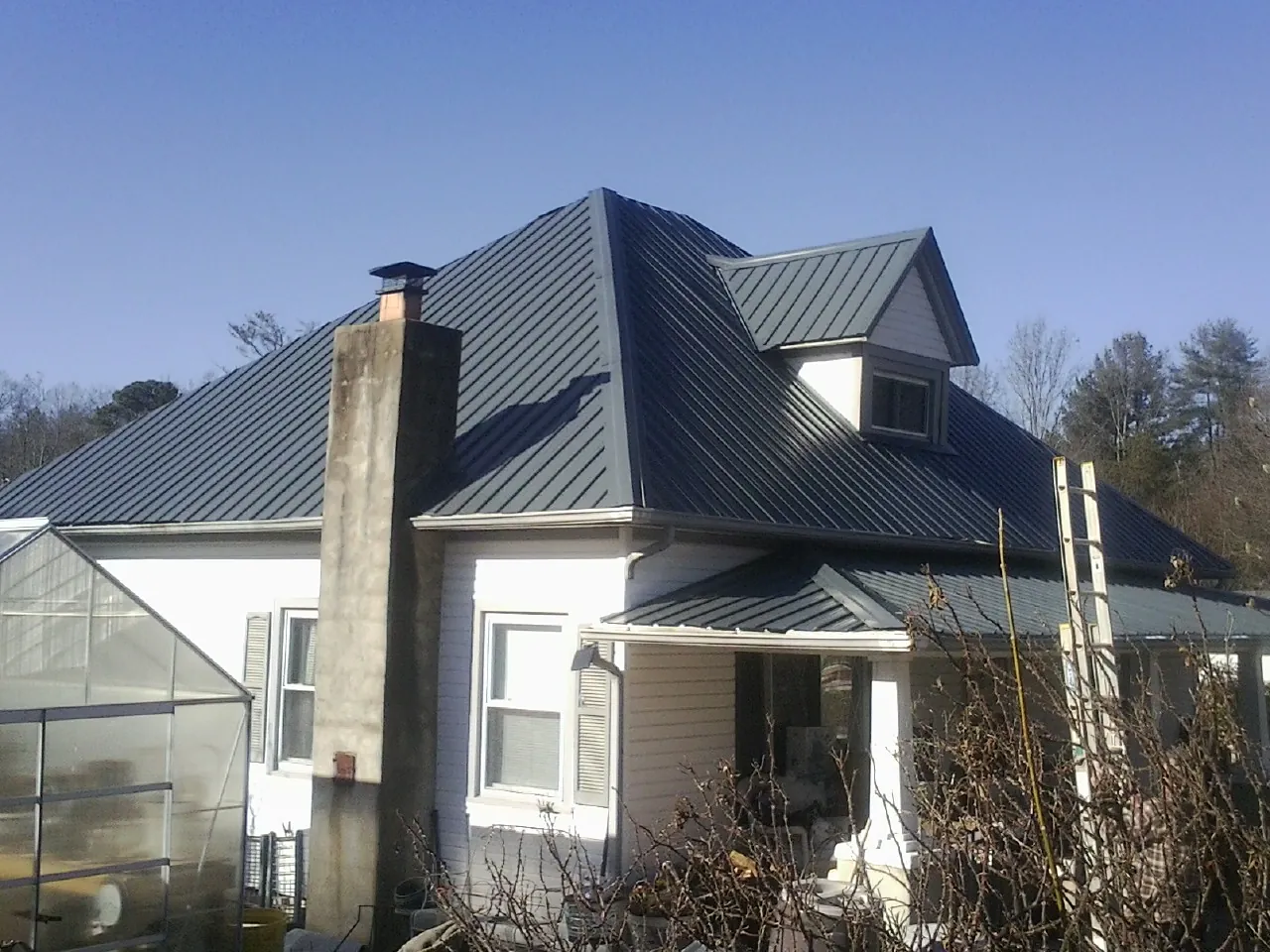 Dark blue standing seam metal roof on a white farmhouse with dormer — Slate & Tile Roof Repair by Roofing Brothers in La Vernia
