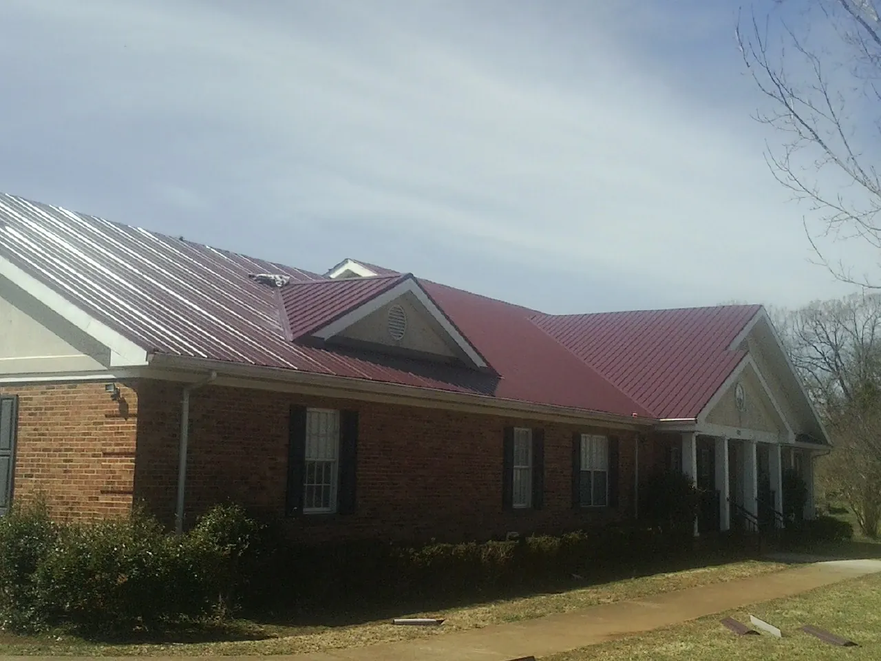 Red metal roof with gabled entries on a long brick building, from a Hail Damage Roof Repair job in La Vernia