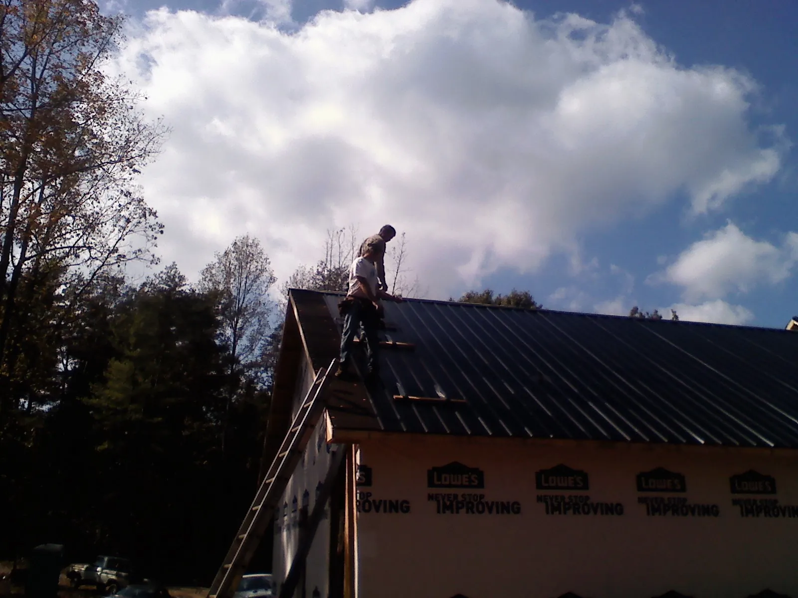 Roofer fastening dark metal panels high against a cloudy sky, from a Roof Inspection job in La Vernia