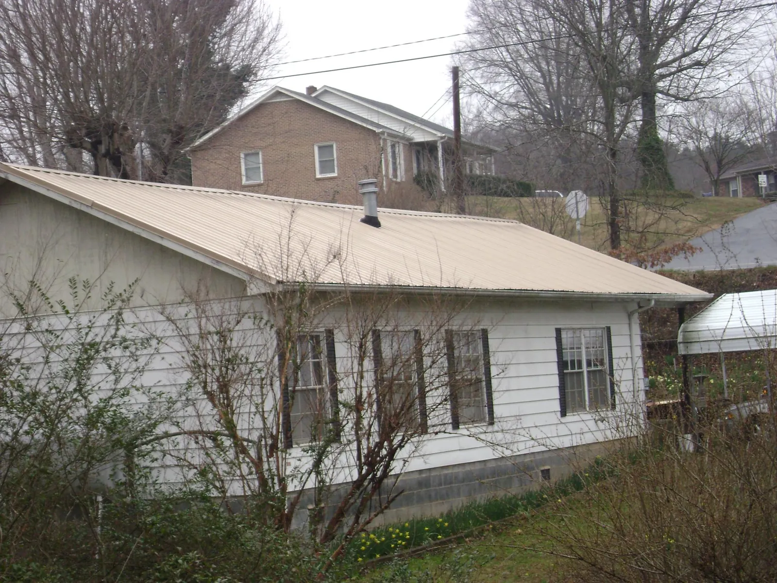 Tan metal roof on a white sided house set into a hillside — Commercial Roofing by Roofing Brothers in La Vernia
